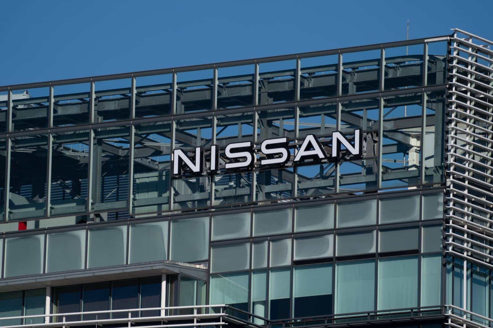 The Nissan name in white capitals mounted on the glass and steel facade of the company's headquarters against a clear blue sky