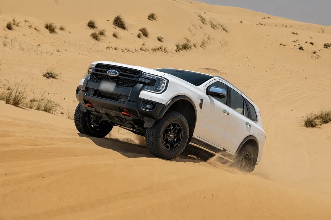 White Ford Everest angled nose-down on the face of a sand dune, front wheels turned, sand spilling away beneath it
