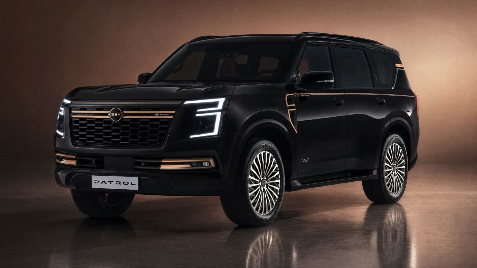 A black Nissan Patrol 75th Anniversary edition in a studio, front three-quarter, with copper-gold bars across the grille and fog lamps, a copper-gold line along the shoulder and multi-spoke wheels