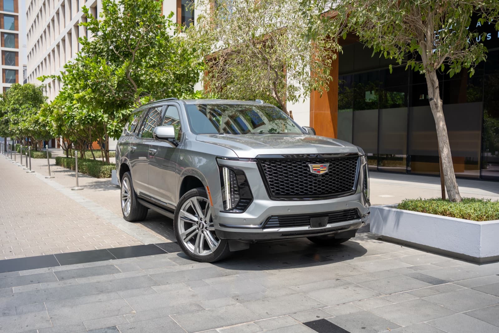 Cadillac Escalade Sport Platinum in silver, photographed from the front three-quarter angle in a shaded Dubai plaza.
